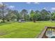 Green backyard featuring a deck and outbuildings, surrounded by lush trees and landscaping at 5849 Rocking Chair Dr, Youngsville, NC 27596