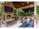 Covered outdoor living space with a stone fireplace, TV, built-in grill, countertop bar, and comfortable seating at 8904 Milden Hall Ct, Raleigh, NC 27615