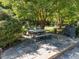 Outdoor stone patio with dining table, seating, and grill shaded by mature trees in landscaped backyard at 1201 Kalworth Rd, Wake Forest, NC 27587