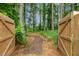 A wooden gate opens to a serene wooded path, inviting exploration and tranquility in nature at 22 Chapman Ct, Wendell, NC 27591