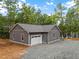 Detached garage with gray siding and a white garage door, nestled in a wooded area at 249 Fisherman Point Rd, Roxboro, NC 27574
