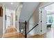 Hallway featuring hardwood floors leading to an open doorway and staircase with wood banister at 4953 Mashpee Ln, Apex, NC 27539