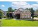 Traditional brick home boasts a manicured lawn and mature trees, enhancing its curb appeal under a bright blue sky at 1010 Mill Pointe Way, Elon, NC 27244