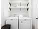 Laundry room with white washer and dryer units, floating shelves, and a dark brown basket at 8722 Macedonia Lake Dr, Cary, NC 27518