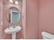 Stylish half bathroom with pink walls, pedestal sink, round mirror, and modern fixtures at 1608 Heritage Links Dr, Wake Forest, NC 27587