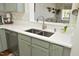 A close up view of the kitchen sink with stainless steel appliances and light green cabinetry with gold hardware at 365 Red Elm Dr, Durham, NC 27713