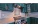 Close up of the stainless steel stove, tiled backsplash, green cabinets, and quartz countertops in this home's kitchen at 973 Rebecca Ln, Siler City, NC 27344