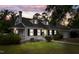 Charming home with manicured lawn, classic white facade, black shutters, and a cozy, lit front porch at dusk at 1001 N Orange Ave, Dunn, NC 28334