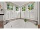 Bright bathroom featuring a large tub, neutral tile, and shuttered windows with decorative valances at 105 Spring Bud Dr, Cary, NC 27513