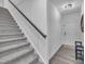 A staircase with carpet steps, a dark handrail, and a white wall is adjacent to wood-look flooring at 81 Paperwhite Pl # 213, Clayton, NC 27527