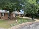 View of brick home with mature shade trees, black shutters, and a covered carport at 609 Malone Ct, Burlington, NC 27215