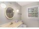 Bright bathroom featuring an oval mirror, unique lighting fixtures, and a beige vanity with a window at 6824 Branton Dr, Cary, NC 27519