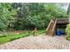 Landscaped backyard with stone patio, decorative fountain, lush greenery, and stairway to a deck at 12212 Ashton Woods Ln, Raleigh, NC 27614