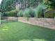 Large backyard with a stone retaining wall and lush green grass, enclosed by a black metal fence at 3129 Elm Tree Ln, Raleigh, NC 27614