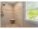 Neutral tiled shower with shower seat, river rock floor, shower wand, and window at 504 S Dixon Ave, Cary, NC 27511