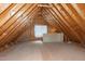 Unfinished attic showcasing wooden framing, plywood flooring, and natural light from a window for potential storage at 4005 Olde Waverly Way, Fuquay Varina, NC 27526