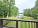 Backyard view featuring a pool and lake surrounded by mature trees, seen from a deck with a railing at 7483 Danford Rd, Burlington, NC 27215