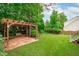 Spacious backyard featuring a pergola with brick patio and manicured lawn surrounded by mature trees at 2003 Red Sage Ct, Apex, NC 27502