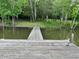 Image of a wooden pier stretching from a grassy shoreline into a calm lake, surrounded by lush green trees at 358 Pool Rock Shores Ln, Henderson, NC 27537