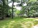 Backyard view highlighting the lush lawn, mature trees, and partially obscured shed for storage at 8 Woodsprite Ct, Durham, NC 27703