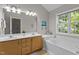 Bright bathroom featuring a double sink vanity, a large mirror, a window, and a soaking tub at 110 Fairchild Downs Pl, Cary, NC 27518