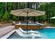 Relaxing in-pool loungers under an umbrella in a modern swimming pool and spa area with stone accents at 113 Hidden Bluff Dr, Chapel Hill, NC 27517