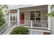 Close up of covered front porch with white railings, a red door with wreath, seating, and lush landscaping at 3923 Napa Valley Dr, Raleigh, NC 27612
