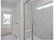 Shower with glass enclosure and marble-patterned tile, small window, and doorway to the carpeted bedroom at 408 Longleaf Glen Lane, Zebulon, NC 27597