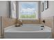 Bright bathroom with a soaking tub, neutral tile surround, and a window overlooking a landscaped yard at 576 Prairie Ln, Lillington, NC 27546