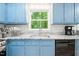 Sunlit kitchen boasts blue cabinets, stainless steel sink, and modern countertops with backyard views at 114 Bonaparte Dr, Hillsborough, NC 27278