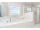 Bright bathroom with marble tile surrounding a tub below a window and a glass-enclosed shower with updated fixtures at 1304 Revolution Cir, Raleigh, NC 27603