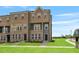 Beautiful exterior view of brick townhomes with manicured lawns and sidewalks under a blue sky at 209 Broomgrove Way, Wake Forest, NC 27587
