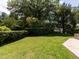 Manicured backyard with lush green lawn, mature trees, hedges, and stone patio seating area at 223 Shadowbrook Dr, Burlington, NC 27215