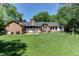 Brick home's backyard with green grass, grill and a patio set among the trees at 1206 Ivy Ln, Raleigh, NC 27609