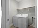 A functional laundry room with a washer, dryer, overhead shelving, and a tiled floor at 249 Salt Cedar Ln, Chapel Hill, NC 27516
