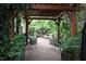 A shaded patio with mature plants, gravel floor, and a seating area beneath a pergola at 3325 Falls River Ave, Raleigh, NC 27614