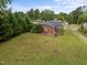 An aerial view of a single-story brick home featuring a spacious yard surrounded by lush greenery and mature trees at 1416 Chestnut St, Roxboro, NC 27573