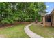 Brick home backyard with a paved walkway, lush greenery, mature trees, and a patio area at 46 Spring Haven Ln, Willow Springs, NC 27592