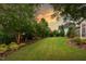Expansive backyard with lush green lawn, mature trees, and manicured landscaping under a golden sunset at 109 Big Timber Path, Holly Springs, NC 27540