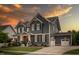 Two-story home featuring gray siding, a well-manicured lawn, and a three-car garage under a colorful sunset at 109 Big Timber Path, Holly Springs, NC 27540
