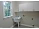 Bright laundry room with a deep utility sink, ample storage cabinets, and a large window offering natural light at 1104 Barrow Nook Ct, Apex, NC 27502