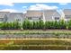 View of gray homes from a pond featuring a retaining wall and green bushes at 113 Mazarin Ln, Cary, NC 27519