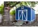 Charming blue shed featuring white trim, a ramp, and a loft window, nestled beside a mature tree with wooden directional signs at 2805 Fayetteville St, Durham, NC 27707