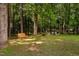 Secluded backyard with a wooden bench, a fire pit, and several chairs surrounded by lush greenery and mature trees at 60 Morning Mist Dr, Garner, NC 27529