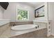 Elegant soaking tub with tile surround, shelving, and a sunny window at 101 Eden Glen Dr, Holly Springs, NC 27540