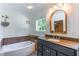 Bathroom featuring a white soaking tub with tile surround and a granite-topped vanity with framed mirror at 5625 Church Rd, Graham, NC 27253