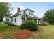 Side view of a white farmhouse featuring a green roof, a partial wrap-around porch, and a landscaped yard at 6447 Beulah Church Rd, Liberty, NC 27298