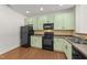 Kitchen features light green cabinets, modern black appliances, and hardwood flooring at 1120 Renewal Pl # 111, Raleigh, NC 27603