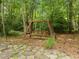 Backyard area with a wooden swing set nestled amongst trees and ground cover on top of stone pavers at 18 Acornridge Ct, Durham, NC 27707