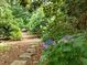 Lush backyard landscaping featuring a stone path, flowering bushes, mature trees, and ground cover at 18 Acornridge Ct, Durham, NC 27707